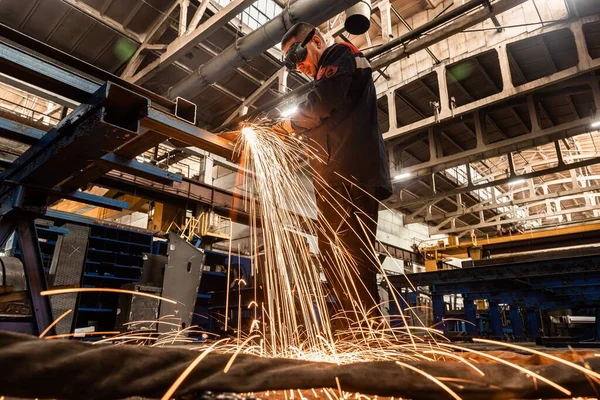 Bir fabrika işçisi, bir üretim hangarının zeminine karşı koruyucu bir maske takan kaynak makinesiyle metal kaynak yapıyor.. — Stok fotoğraf