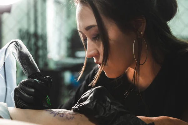 Un tatoueur professionnel fait un tatouage noir et blanc sur une jambe de femme, en appliquant à l'encre. Le processus de tatouage de la peau. — Photo