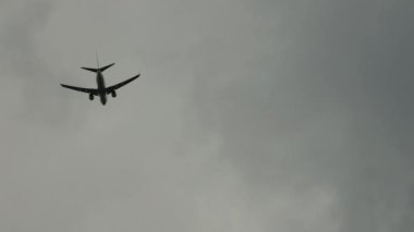 Üzerimizden uçan bir yolcu uçağı bulutlu bir gökyüzünün arka planına inmeye hazırlanıyor.