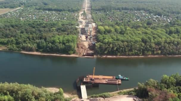 Vista superior de la construcción de un puente sobre el río. Disparos aéreos desde un dron de un sitio de construcción, equipos especiales y trabajadores, así como cruces de puentes — Vídeo de stock