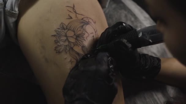 Egy profi tetováló művész fekete-fehér tetoválást készít egy női lábon, tintával. A bőr tetoválásának folyamata.