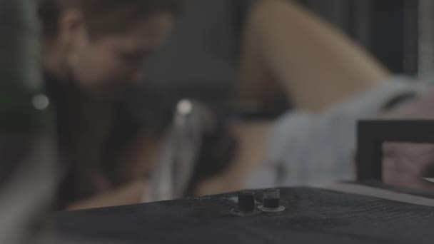 Egy profi tetováló művész fekete-fehér tetoválást készít egy női lábon, tintával. A bőr tetoválásának folyamata.