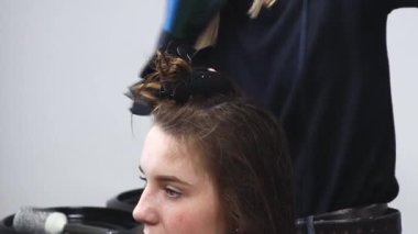 Usta kadın kuaför bir güzellik salonunda yıkandıktan sonra saç kurutma makinesiyle kızın saçını kurutuyor..