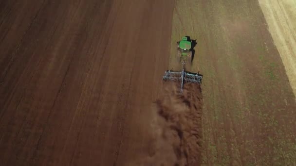 El dron 4K que dispara desde arriba del tractor trabaja en el campo y araña el suelo, levantando polvo. Preparación y cultivo del suelo para la próxima temporada de cosecha — Vídeo de stock