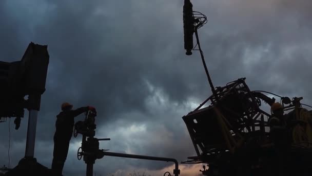 Een medewerker in overalls en een helm is bezig met reparaties en onderhoud van een oliebron. Silhouet op de achtergrond van de avondhemel — Stockvideo