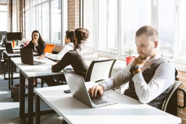 Gündelik giyinen genç iş adamları ofiste birlikte çalışıyorlar. Ekip iş başında.