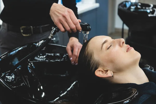 Master parrucchiere donna lava delicatamente i capelli delle ragazze con shampoo e balsamo prima di styling in un salone di bellezza. — Foto Stock