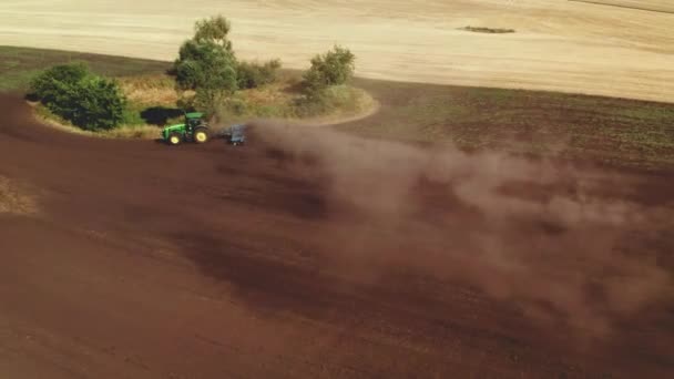 El dron 4K que dispara desde arriba del tractor trabaja en el campo y araña el suelo, levantando polvo. Preparación y cultivo del suelo para la próxima temporada de cosecha — Vídeo de stock
