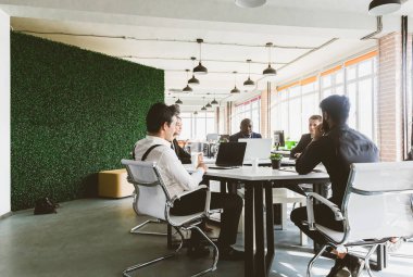 Ofis masasında iş arkadaşlarıyla otururken çalışan ve iletişim kuran bir grup genç iş adamı. iş toplantısı