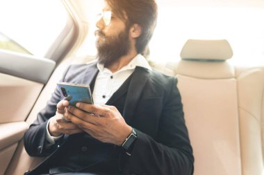 Gözlüklü ve sakallı şık Hindu patron arabanın arka koltuğunda telefonla çalışıyor. Güvenli ve rahat iş seyahati