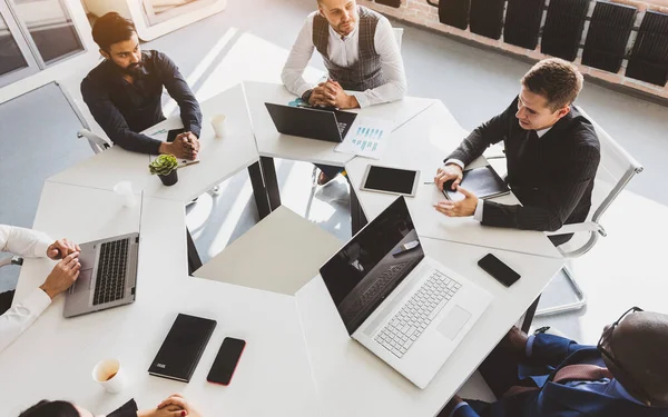 Ofis masasında iş arkadaşlarıyla otururken çalışan ve iletişim kuran bir grup genç iş adamı. İş toplantısı. Masaüstü görünümü.