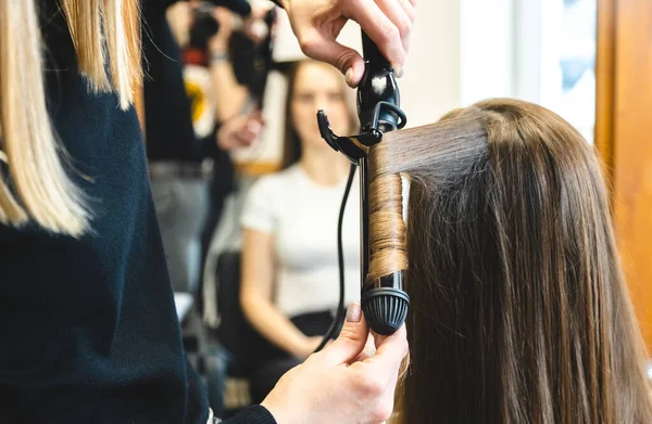 La peluquera maestra riza suavemente a la chica rizadora en un salón de belleza. Peinado del cabello — Foto de Stock