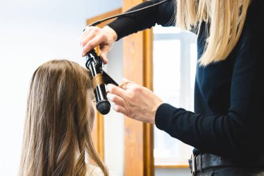 Usta kadın kuaför bir güzellik salonunda saç kıvıran kızı nazikçe kıvırtır. Saç şekillendirme