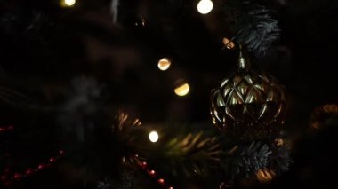 Noel ağacının dallarındaki Noel süslemeleri, arka plandaki çelenk ışıklarının sıcak ışıklarıyla titreşiyor..