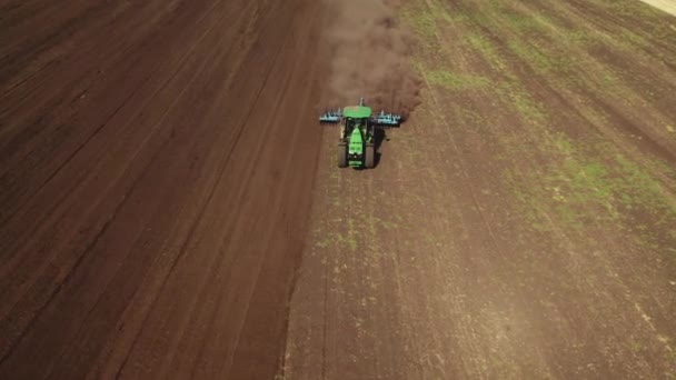 4K drone disparando de cima do trator funciona no campo e arado o chão, levantando poeira. Preparação e cultivo do solo para a próxima época de colheita — Vídeo de Stock