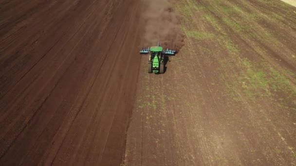 El dron 4K que dispara desde arriba del tractor trabaja en el campo y araña el suelo, levantando polvo. Preparación y cultivo del suelo para la próxima temporada de cosecha — Vídeo de stock