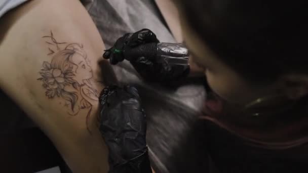 한 여성 이 예술가에게 문신을 새기고, 스튜디오에서 문신을 하고, 몸에 문신을 합니다. 클로즈업 — 비디오