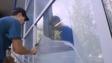 Erkek bir uzman caddedeki bir bankanın camlarını temizler ve yıkar. Temizlik servisi