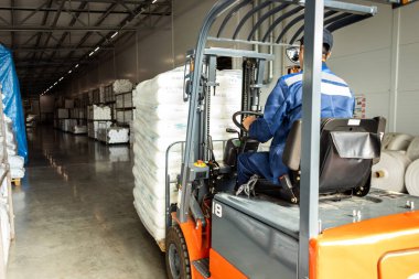 Forklift kullanan bir adam büyük bir depoda çalışır ve bir çanta dolusu hammaddeyi boşaltır.