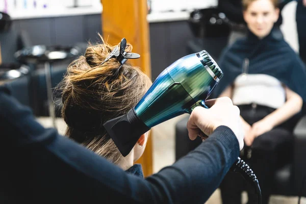Master žena kadeřnice vysuší dívky vlasy s fénem a hřebeny po mytí v salonu krásy — Stock fotografie