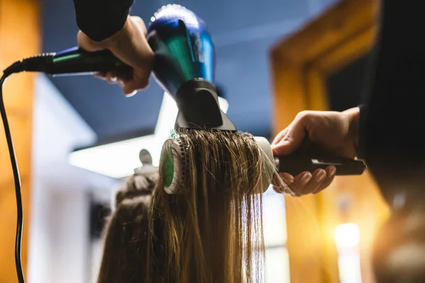 Mester nő fodrász szárítja a lányok haját egy hajszárítóval és fésülködik mosás után a szépségszalonban. — Stock Fotó