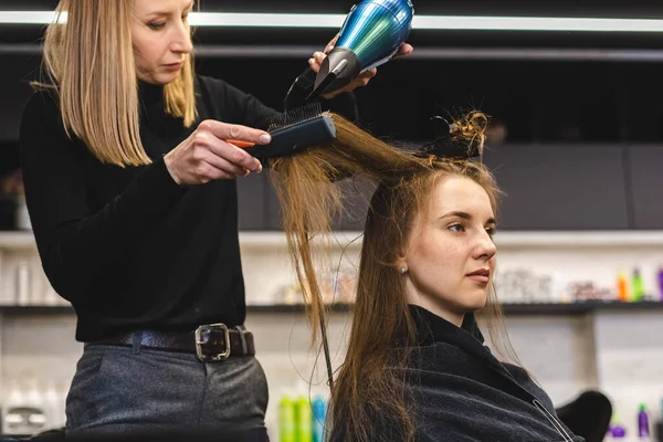 Mester nő fodrász szárítja a lányok haját egy hajszárítóval és fésülködik mosás után a szépségszalonban. — Stock Fotó