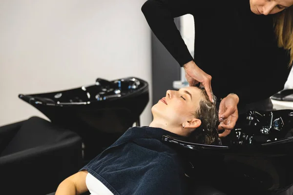 Friseurmeisterin wäscht die Haare der Mädchen sanft mit Shampoo und Conditioner, bevor sie sich in einem Schönheitssalon stylt. — Stockfoto