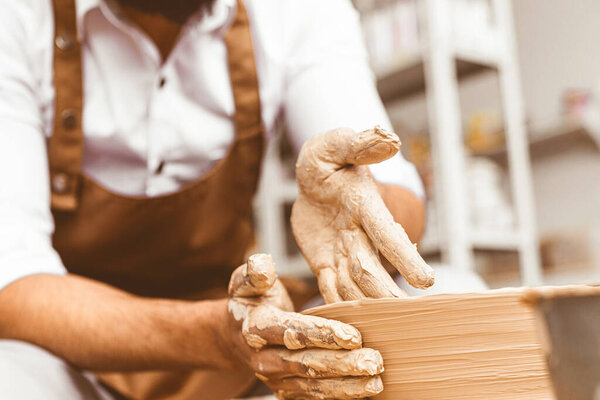 A young male potter works in his workshop on a potters wheel and makes clay products. Close-up of hands