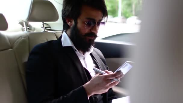 Elegante empresario indio en un coche funciona y utiliza un teléfono inteligente. Convocatorias de empresas y movilidad en coproceso — Vídeos de Stock