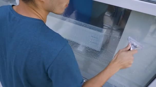 Uno specialista di sesso maschile pulisce e lava le finestre di una banca sulla strada. Servizio di pulizia — Video Stock