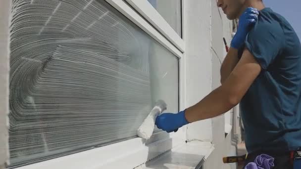 Trabajador masculino profesional en overoles limpia hábilmente las ventanas con productos químicos especiales de cerca — Vídeo de stock
