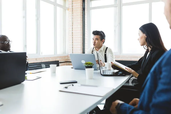 Gruppo di giovani imprenditori che lavorano e comunicano mentre sono seduti alla scrivania dell'ufficio insieme ai colleghi seduti. riunione d'affari Foto Stock