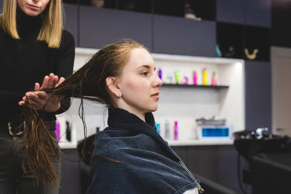 Friseurmeisterin trägt nach dem Waschen der Mädchen im Schönheitssalon vorsichtig eine spezielle Haarspülung auf. — Stockfoto