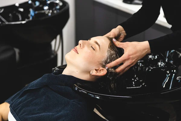 Maître femme coiffeur lave doucement les cheveux des filles avec shampooing et revitalisant avant de coiffer dans un salon de beauté. — Photo