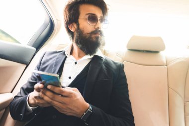 Gözlüklü ve sakallı şık Hindu patron arabanın arka koltuğunda telefonla çalışıyor. Güvenli ve rahat iş seyahati