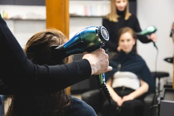 Master woman hairdresser dries the girls hair with a hairdryer and combs after washing in the beauty salon