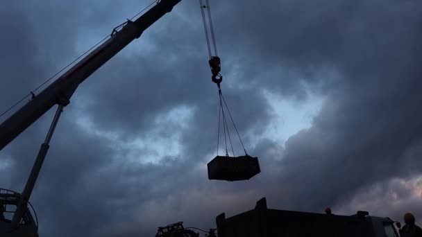 The silhouette of a working truck crane and a special vehicle for servicing oil wells dismantles equipment against the background of the evening sky — Stock Video