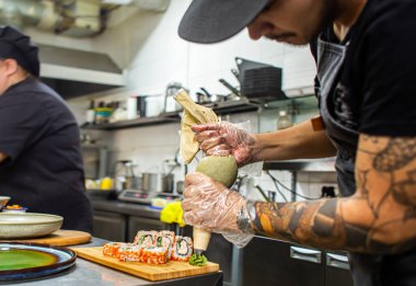 Erkek aşçılar restoranın mutfağında suşi hazırlıyorlar. Şef çörekleri wasabi ile süslüyor.