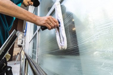 Profesyonel bir temizlik servisinin çalışanı ön cephe ve pencereleri özel cihazlarla yıkar.