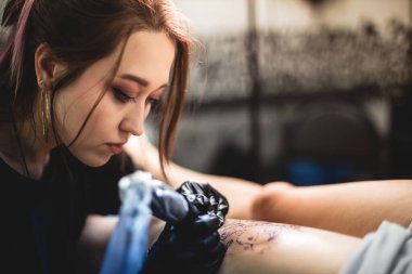 Profesyonel kadın dövme sanatçısı stüdyoda dövme yapıyor, yakın plan. Karanlık fotoğrafçılık