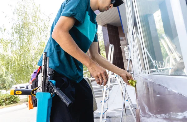 En anställd på en professionell städservice i overaller tvättar fasaden och fönster med speciella enheter — Stockfoto