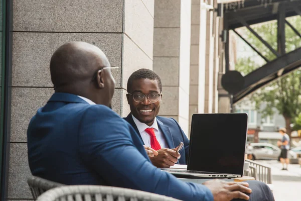 Deux hommes d'affaires afro-américains à la peau foncée en costumes et lunettes avec mallettes s'assoient à une table dans un café de la ville en plein air. — Photo