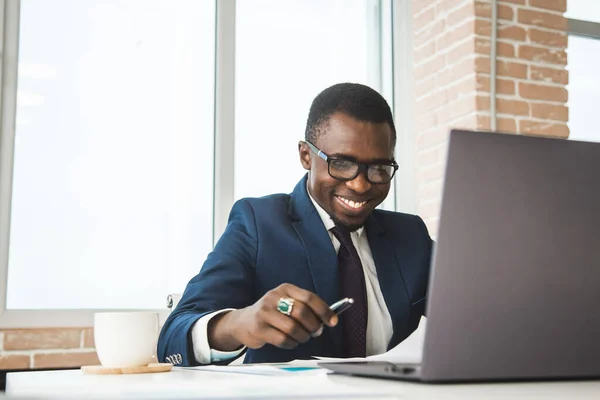Retrato de un afroamericano en la oficina. Hombre negro en un traje de negocios trabajando en un portátil —  Fotos de Stock
