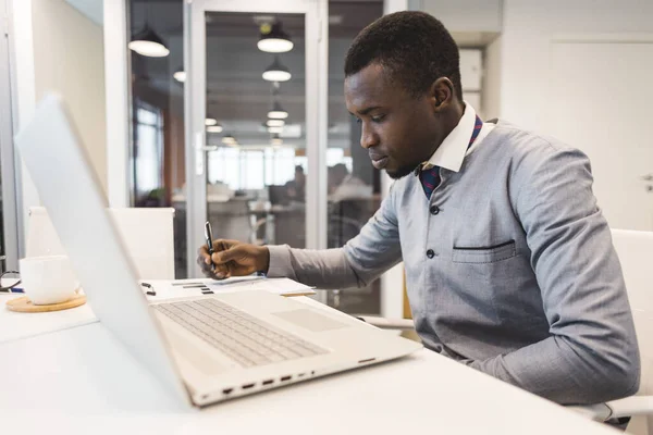 Retrato de un afroamericano en la oficina. Hombre negro en un traje de negocios trabajando en un portátil —  Fotos de Stock