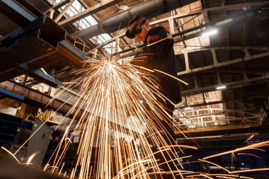 Bir fabrika işçisi, bir üretim hangarının zeminine karşı koruyucu bir maske takan kaynak makinesiyle metal kaynak yapıyor..