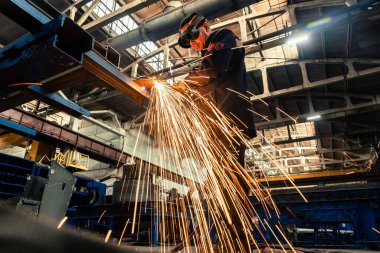 Bir fabrika işçisi, bir üretim hangarının zeminine karşı koruyucu bir maske takan kaynak makinesiyle metal kaynak yapıyor..