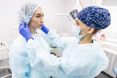 Dişçi konsepti. Profesyonel diş hizmetleri ve acısız modern ekipmanlar. Doktor asistanı hastayı tedavi için hazırlar ve giydirir.