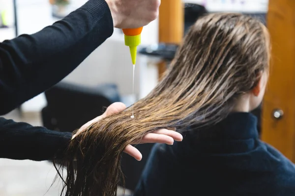 Maestra peluquera mujer aplica cuidadosamente un acondicionador especial para el cabello después de lavar la cabeza de las niñas en un salón de belleza — Foto de Stock