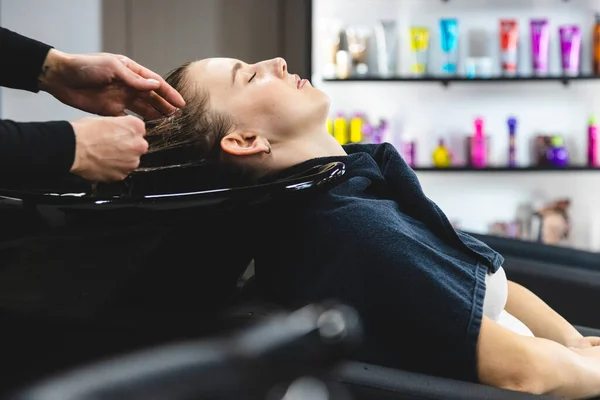 Master parrucchiere donna lava delicatamente i capelli delle ragazze con shampoo e balsamo prima di styling in un salone di bellezza. — Foto Stock