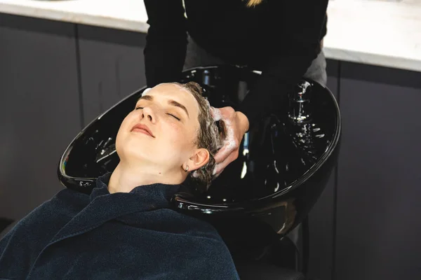 Master parrucchiere donna lava delicatamente i capelli delle ragazze con shampoo e balsamo prima di styling in un salone di bellezza. Foto Stock